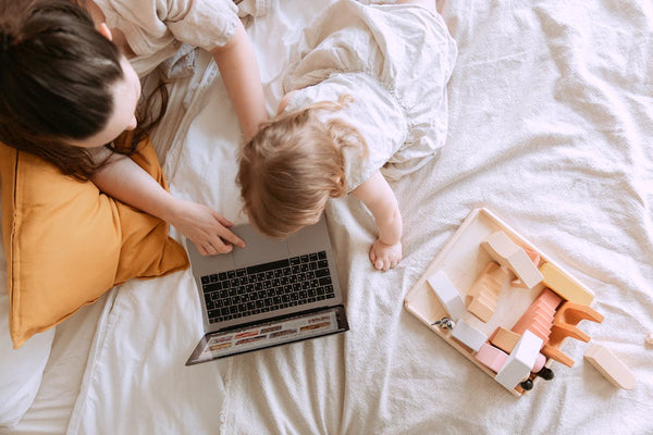 A mother and her child on a bed watching something on her laptop
